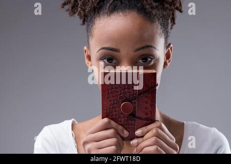 Carino giovane donna nera peering sopra un caseificio legato in pelle sta tenendo in mano il viso guardando la fotocamera con gli occhi grandi in un primo piano in un portrai tagliato Foto Stock