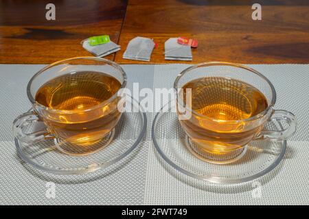 Due tazze di tè in tenuto su un tavolo con bustine di tè e spazio di copia sullo sfondo Foto Stock