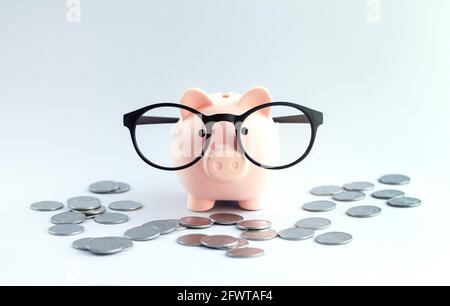 Piggybank con occhiali da vista sul tavolo da ufficio con mucchio di monete. Risparmio di denaro o concetto di risparmio Foto Stock