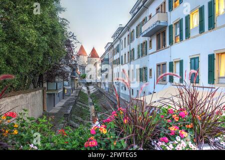 Scena di strada lungo un canale d'acqua nel centro storico di Yverdon les Bains, Svizzera, con le torri del Castello di Yverdon sullo sfondo. Foto Stock