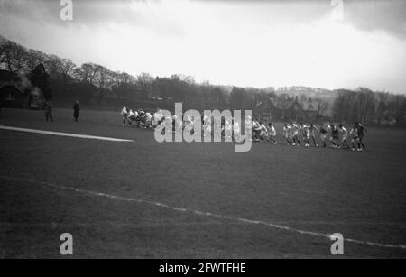1951, storico, fuori in un grande campo sportivo, un gruppo di scolari formazione all'inizio di una corsa o di una corsa di fondo. Foto Stock