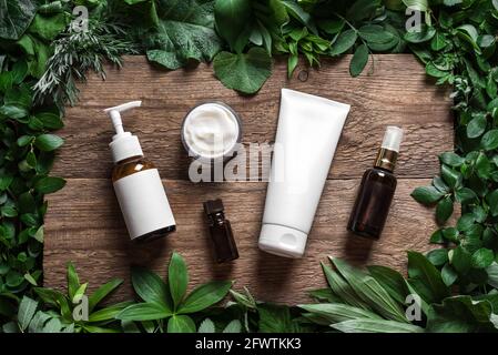 Prodotti cosmetici per la cura della pelle (lozione per il corpo, shampoo per capelli, crema per il viso, olio essenziale) su foglie verdi come sfondo, vista dall'alto. Eco bellezza naturale e org Foto Stock