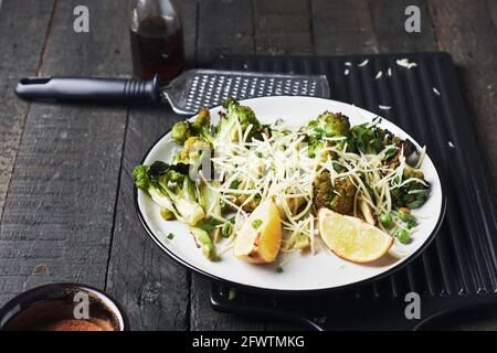 Broccoli arrosto con formaggio e limone su un tavolo di legno scuro. Foto Stock