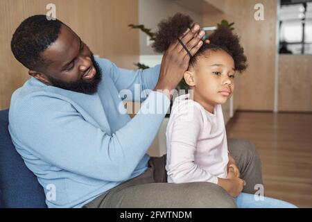 Il padre afroamericano spazzolando facendo la pettinatura per la sua figlia giovane Foto Stock