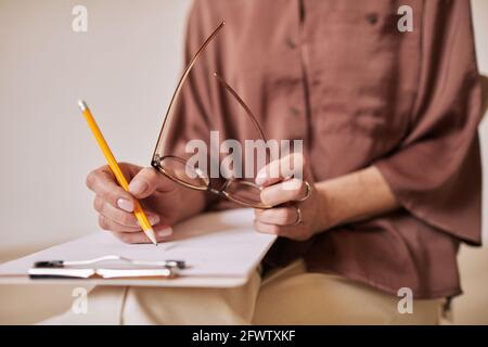 Primo piano minimo di una psicologa femminile irriconoscibile che scrive sulla clipboard durante la sessione di terapia nel gruppo di supporto, spazio di copia Foto Stock