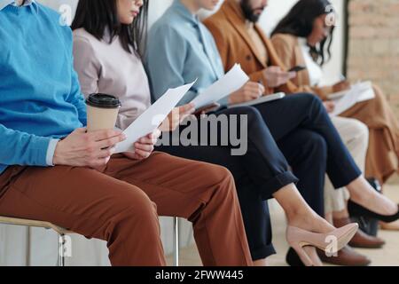 Immagine ritagliata di candidati interracial seduti con i documenti in fila e preparandosi per il colloquio di lavoro Foto Stock