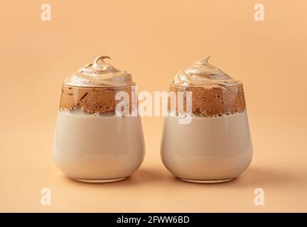 Due bicchieri di bevanda a base di caffè con latte e schiuma montata su sfondo arancione. Foto Stock