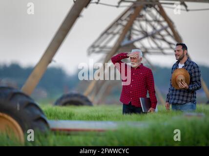 Farmers standing in field looking surveying. Two men next to center pivot irrigation system modern agriculture. Foto Stock