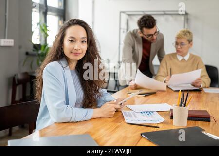 Manager femminile di successo che lavora con carte e dati online contro due colleghi Foto Stock