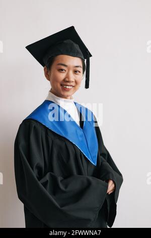 Verticale vita in su ritratto di giovane donna asiatica che indossa una graduazione accappatoi e sorridendo alla macchina fotografica Foto Stock