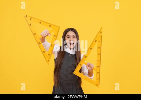 felice bambino tenere testa triangolo matematico regolo a scuola su sfondo giallo, l'istruzione Foto Stock