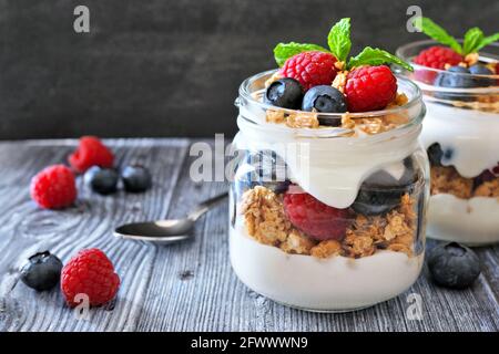 Parfait sani di mirtillo e lampone in vasetti di muratore. Primo piano della scena del tavolo su sfondo rustico scuro. Foto Stock