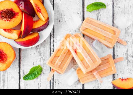 Pop-sicles di yogurt alla pesca estivo, scenario da tavolo con vista dall'alto su uno sfondo rustico di legno bianco Foto Stock