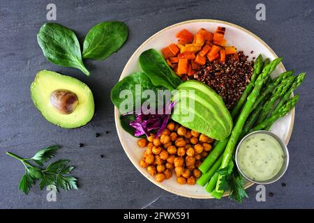 Ciotola di Buddha sana con asparagi, quinoa, patate dolci, ceci e avocado. Vista dall'alto su uno sfondo di ardesia scuro. Foto Stock