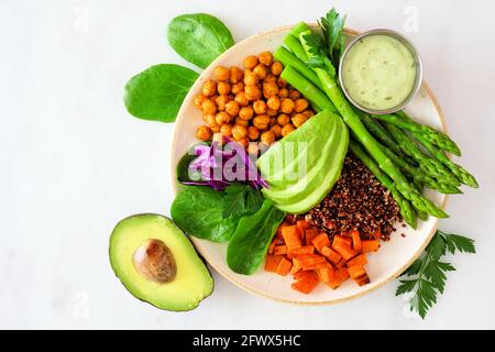 Ciotola di Buddha sana con asparagi, quinoa, patate dolci, ceci e avocado. Vista dall'alto su uno sfondo di marmo bianco. Foto Stock