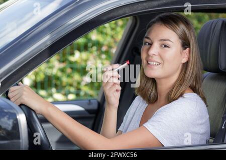 giovane donna di buon aspetto che applica rossetto in auto Foto Stock