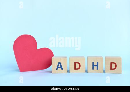 Amare e sostenere i bambini con ADHD o concetto di disturbo da deficit di attenzione iperattività. Lettere ADHD su blocchi di legno accanto a una forma a cuore rosso Foto Stock