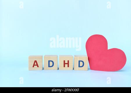 Amare e sostenere i bambini con ADHD o concetto di disturbo da deficit di attenzione iperattività. Lettere ADHD su blocchi di legno accanto a una forma a cuore rosso Foto Stock