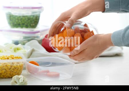 Donna che mette le carote in contenitore di plastica in cucina, closeup Foto Stock