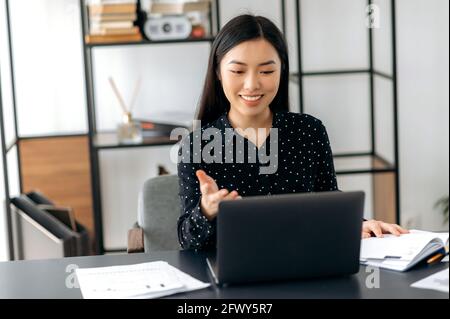 Carismatico fidato di successo asiatico business lady, freelancer, manager, utilizzando il laptop, parlare in videoconferenza con il cliente o collega, discutere di progetto di business, gesturing con la mano, sorridendo Foto Stock