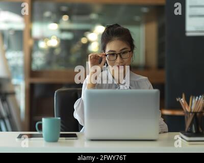 Ritratto di donna d'affari con occhiali concentrandosi sul suo lavoro con computer portatile in ufficio Foto Stock