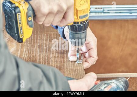 L'operatore avvita l'angolo in metallo sulla tavola di legno con un trapano wireless montaggio nuova cucina esterna in cortile cottage vista ravvicinata estrema Foto Stock