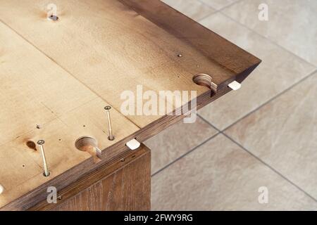 Montaggio di un grande tavolo da pranzo in legno con i connettori del piano di lavoro e. avviti all'aperto durante la giornata di sole, vista ravvicinata Foto Stock