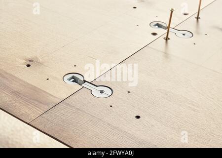 Montaggio di un grande tavolo da pranzo in legno con connettori installati sul piano di lavoro e si sviti all'aperto durante la giornata di sole, vista ravvicinata Foto Stock