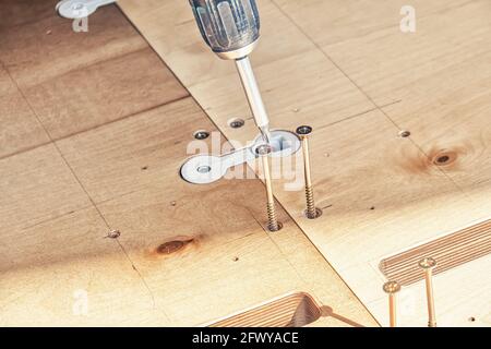 Il dipendente assembla le nuove viti di rotazione del tavolo da pranzo in legno con l'elettricità avvitatore all'aperto nelle giornate di sole closeup estremo Foto Stock