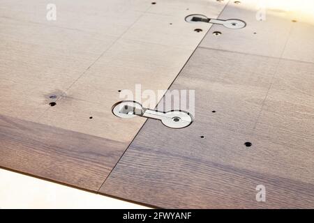 Montaggio di un grande tavolo da pranzo in legno con connettori installati sul piano di lavoro e si sviti all'aperto durante la giornata di sole, vista ravvicinata Foto Stock