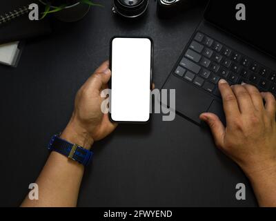 Vista dall'alto della mano di un uomo d'affari che lavora con la tastiera del tablet e. tenere lo smartphone in un'area di lavoro buia Foto Stock