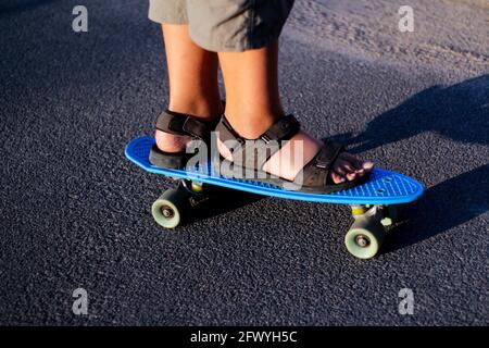 Sfida lo skater che si muove lungo la strada asfaltata su uno skateboard giallo con sandali neri. Alcune delle gambe si trovano su uno skateboard da vicino. Giovani acti sportivi Foto Stock