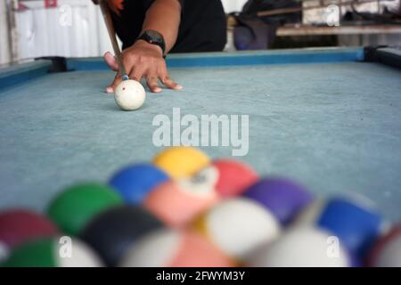 le mani degli uomini giocano a biliardo su un tavolo blu con moquette. un ritratto di un giocatore professionista con una palla da biliardo sfocata in primo piano. il primo passo di Foto Stock