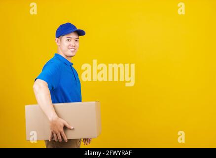 Ritratto eccitato attraente consegna felice uomo logistico sorriso in piedi indossando t-shirt blu e tappo uniforme contenitore di tenuta pacchi guardando fotocamera, prigioniero Foto Stock