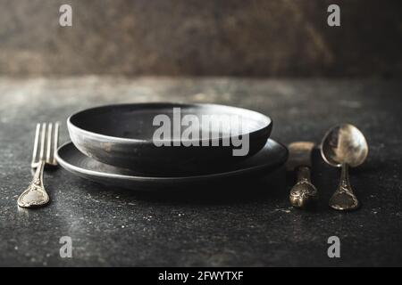 Piatto vintage vuoto con coltello argentato, cucchiaio e forchetta su tavola nera. Foto Stock
