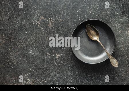 Piatto vintage vuoto con cucchiaio argento su tavolo nero. Vista dall'alto. Foto Stock