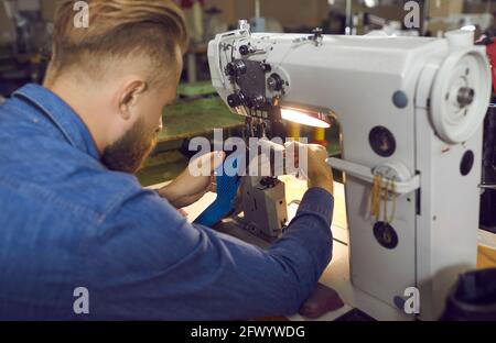 Lavoratore della fabbrica di calzature seduto al tavolo in officina e in uso macchina per cucire scarpe industriali Foto Stock