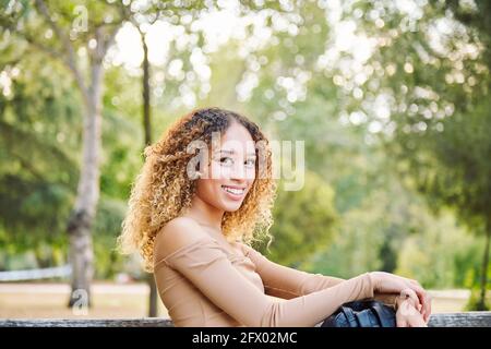 Donna con capelli afro, nella foresta divertendosi felice. Latina ragazza seduta sulla panchina del parco. Foto di alta qualità Foto Stock