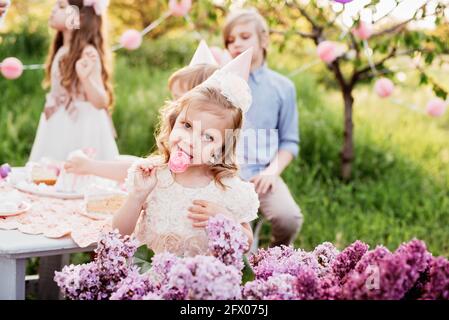 Buon compleanno bambina fare desiderio soffiare candele su torta con decorazione rosa in bellissimo giardino. 4 anni compleanno. bambino mangiare buon compleanno rosa cu Foto Stock