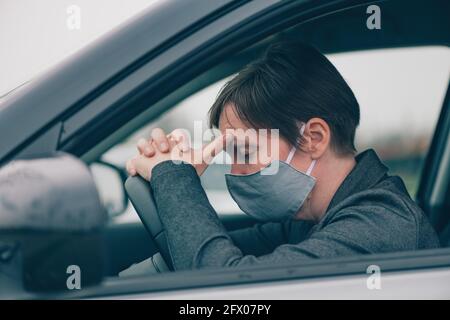 Deluso driver femminile con maschera protettiva seduta in auto durante le pandemie Covid-19, appoggiandosi la testa al volante, selettivo fo Foto Stock