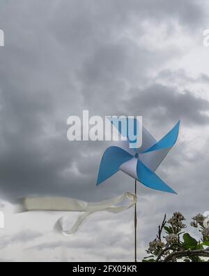 Una pinwheel blu e bianca con un nastro che soffia dentro il vento contro un cielo drammatico con nuvole scure Foto Stock