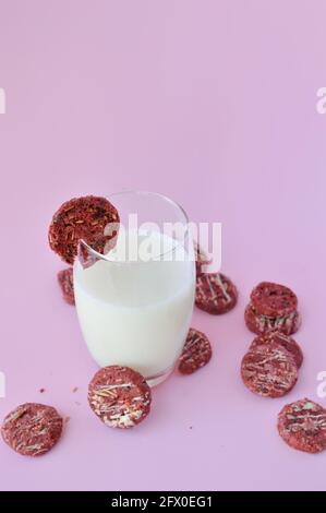 Biscotto rosso su un bicchiere di latte con molti altri sparsi su sfondo rosa Foto Stock