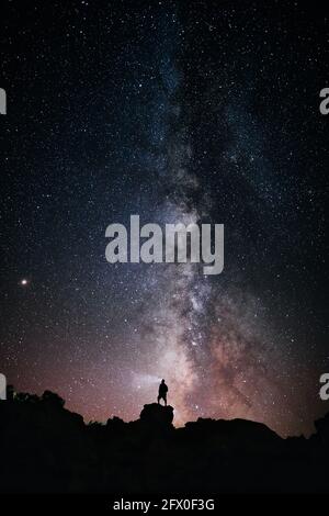 Basso angolo di silhouette di anonimo standing turistico con luce torcia sulla testa sulla scogliera contro il cielo stellato incandescente a. notte Foto Stock
