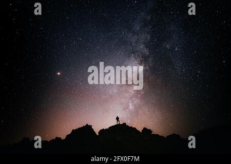 Silhouette di turista anonimo in piedi su scogliera contro stellato incandescente cielo di notte Foto Stock