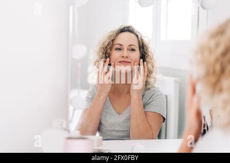 Vista laterale di un giovane maschio autoassicurato in un outfit elegante regolare gli occhiali da sole futuristici mentre ci si trova in uno studio buio con il neon illuminazione Foto Stock
