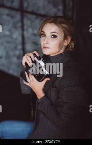 Bella ragazza bionda fotografo in una tuta rigida tiene in mano la vecchia fotocamera retrò. Foto Stock