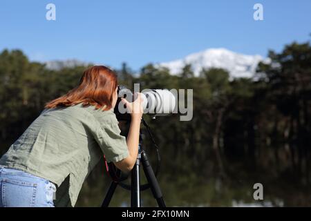 Vista posteriore di un fotografo che scatta foto con teleobiettivo e fotocamera dslr in montagna Foto Stock