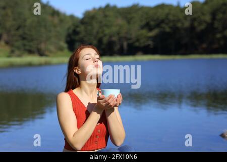 Donna che tiene la tazza di caffè che respira aria fresca in un lago in montagna una giornata di sole Foto Stock