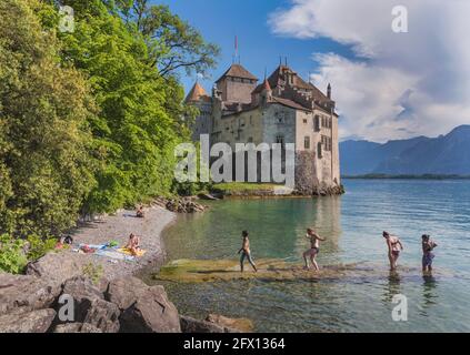 Bagnanti sulla riva del Lago di Ginevra (Lac Leman) accanto al Castello di Chillon, o Castello di Chillon. Veytaux, Cantone di Vaud, Svizzera. Reco scritto Foto Stock