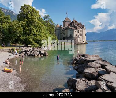 Bagnanti sulla riva del Lago di Ginevra (Lac Leman) accanto al Castello di Chillon, o Castello di Chillon. Veytaux, Cantone di Vaud, Svizzera. Reco scritto Foto Stock